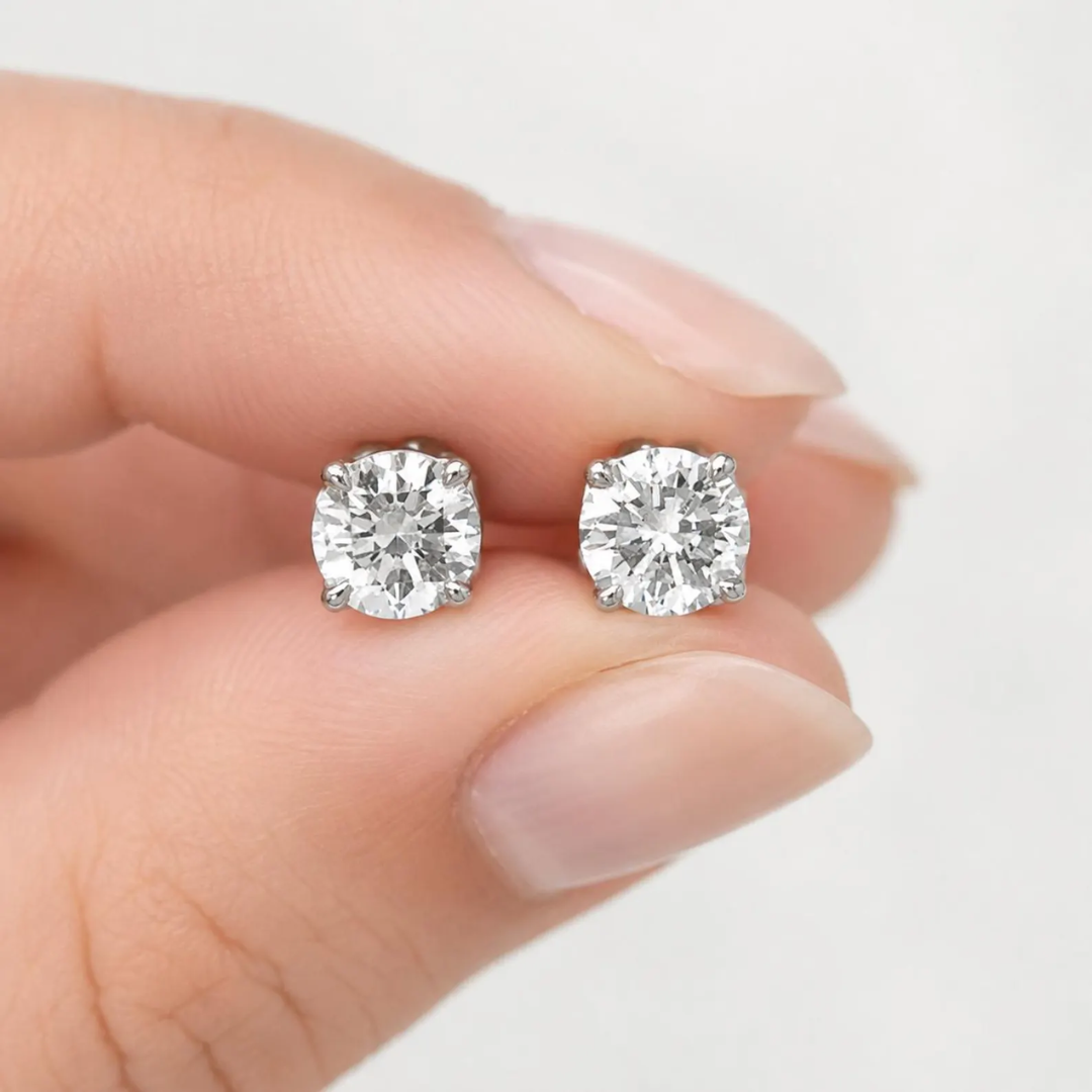 Diamond stud earrings held between two fingers against a neutral background