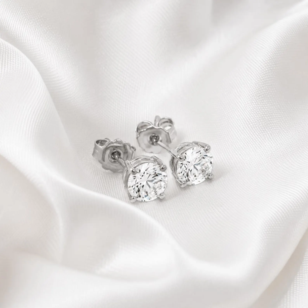 Silver stud earrings with clear gemstones on a white satin background